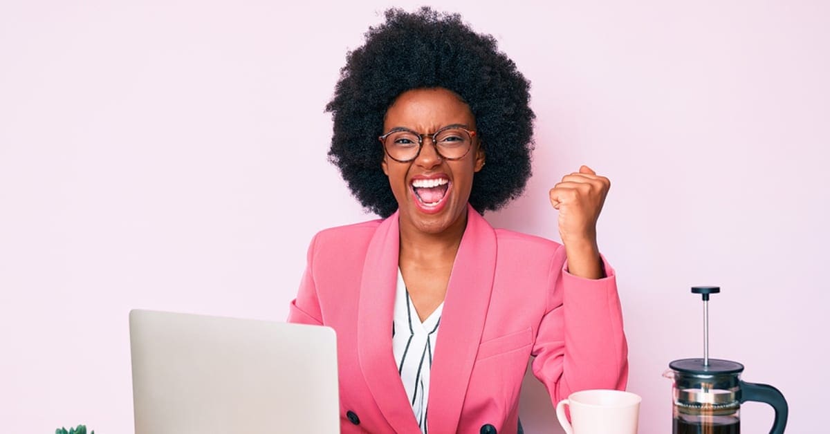 African American Woman in Pink Blazer Posing Smiling in Front of Laptop