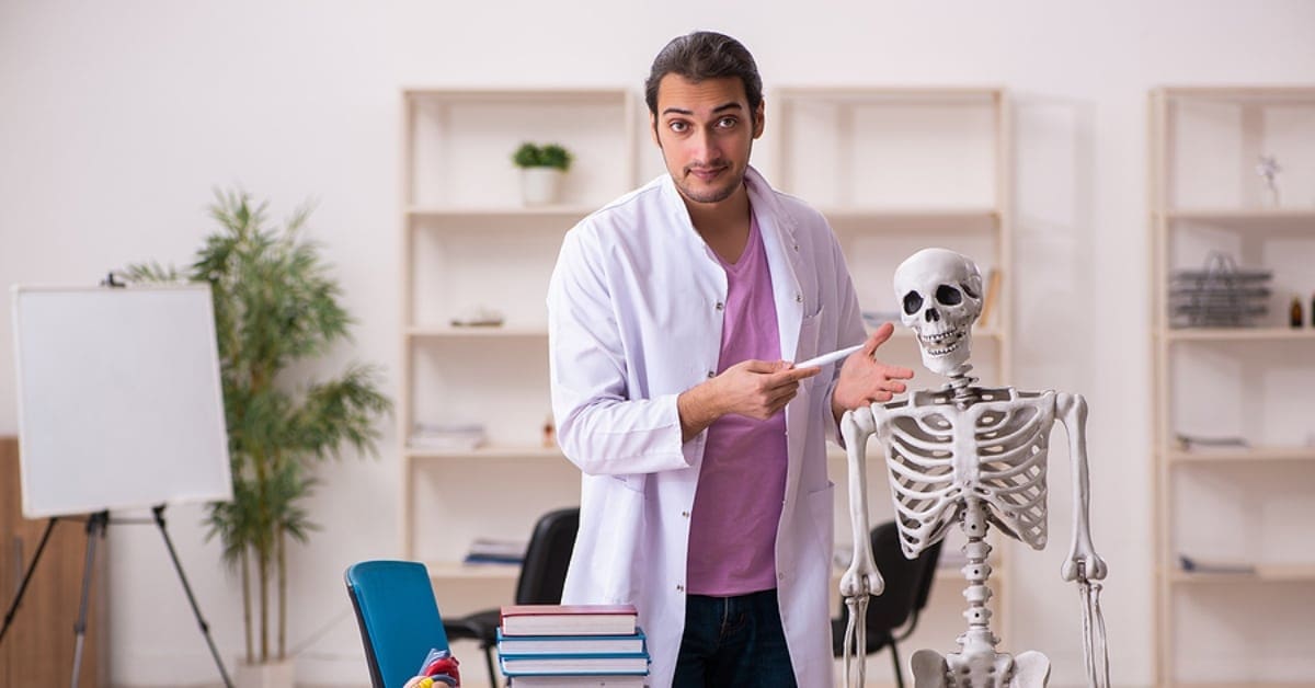 Man Posing in Lab Coat by Human Skeleton Replica