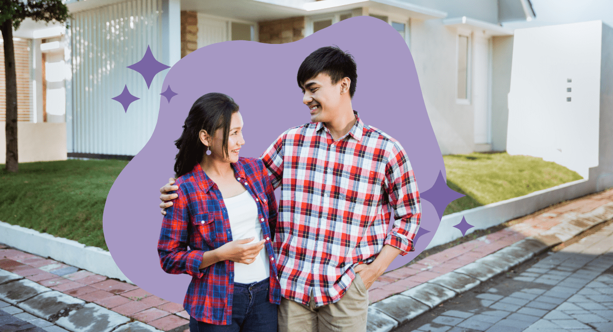 An asian couple looking at each other smiling in front of a house