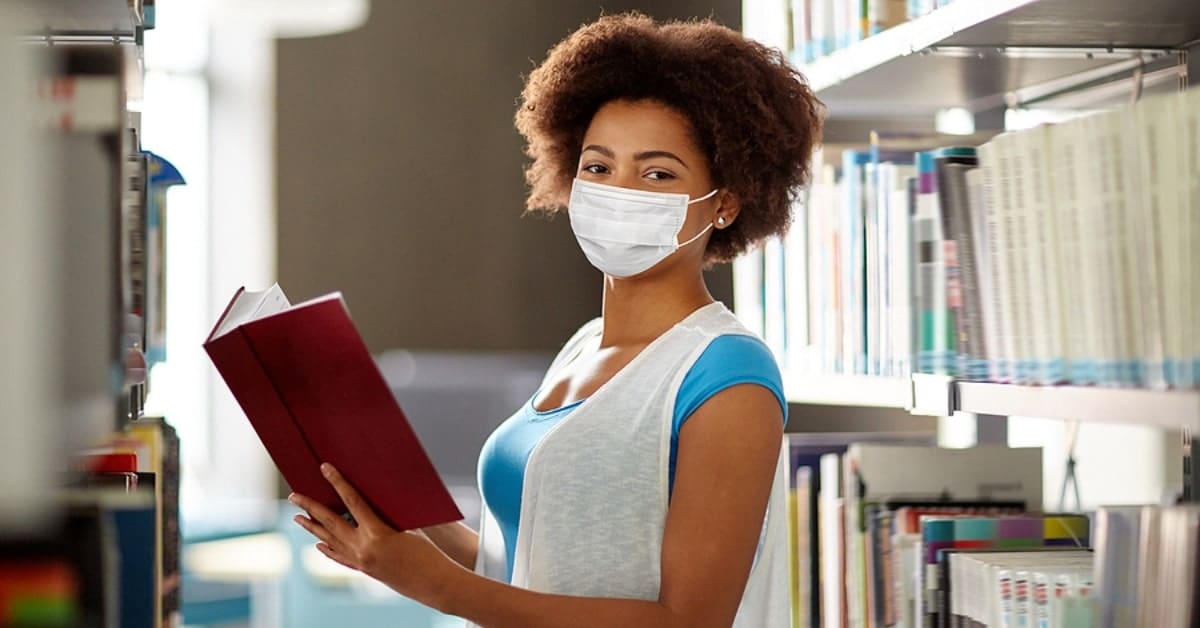 African American Woman Wearing Mask Reading Book Posing in a Library