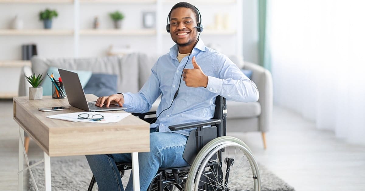 Man in Wheelchair Posing with a Thumbs Up in Front of Laptop