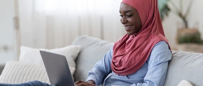 Muslim African American Woman Smiling While Looking Down at Laptop