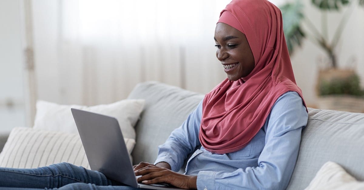Muslim African American Woman Smiling While Looking Down at Laptop