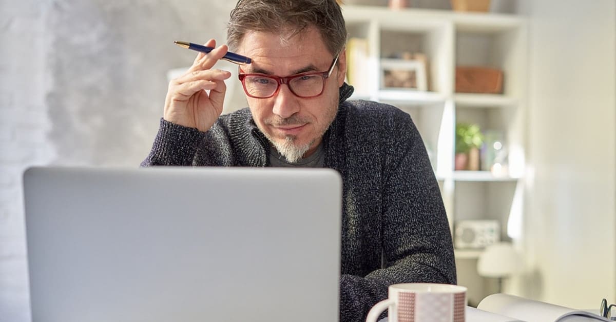 Man Deliberating Looking at Laptop While Holding Pen