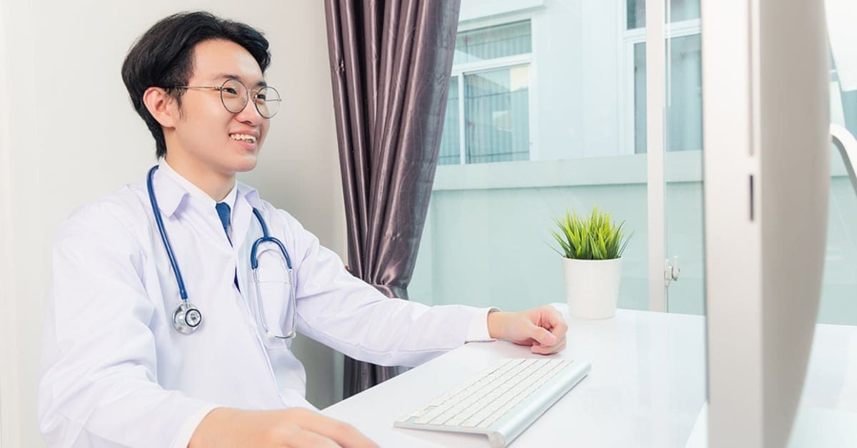 Asian Male Physician Smiling at his Computer Monitor