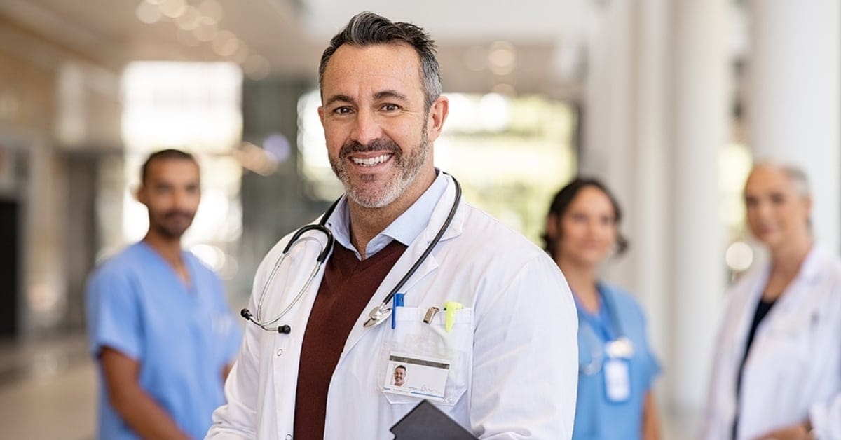 Caucasian Physician Smiling for Camera with other Physicians in the Backdrop