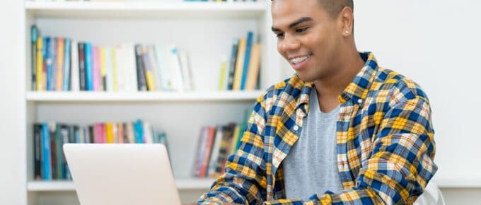 Young Adult Male in Plaid Shirt Smiling While Working on his Laptop