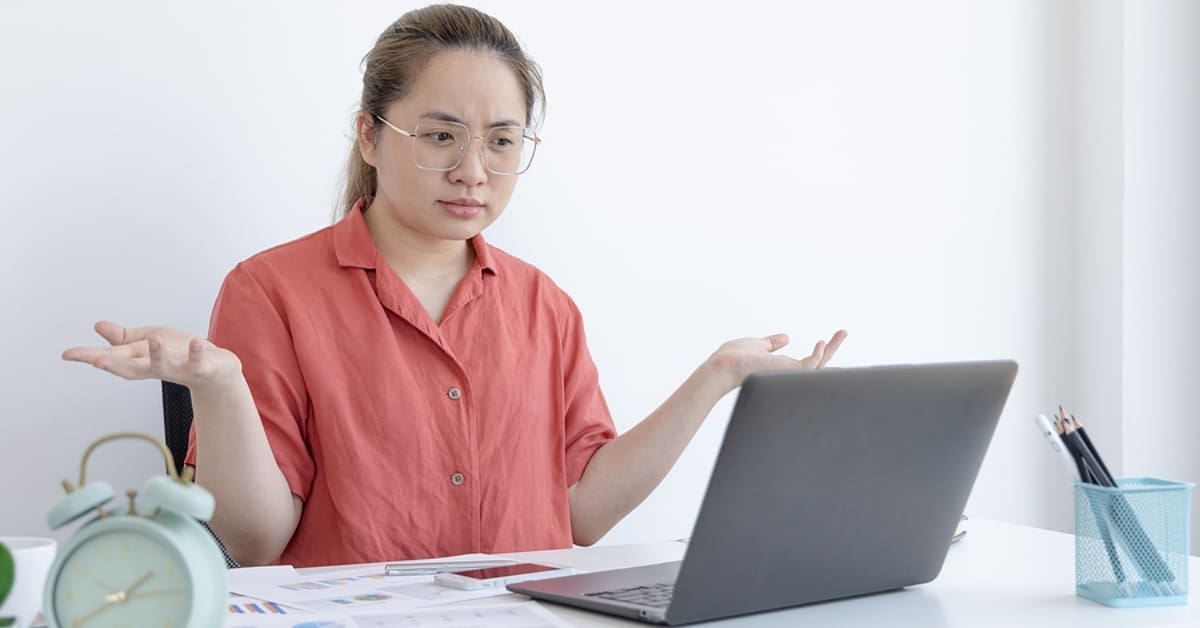 Asian Woman Shrugging While Looking at Laptop