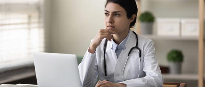 Female Physician Pondering While Sitting in Front of Laptop