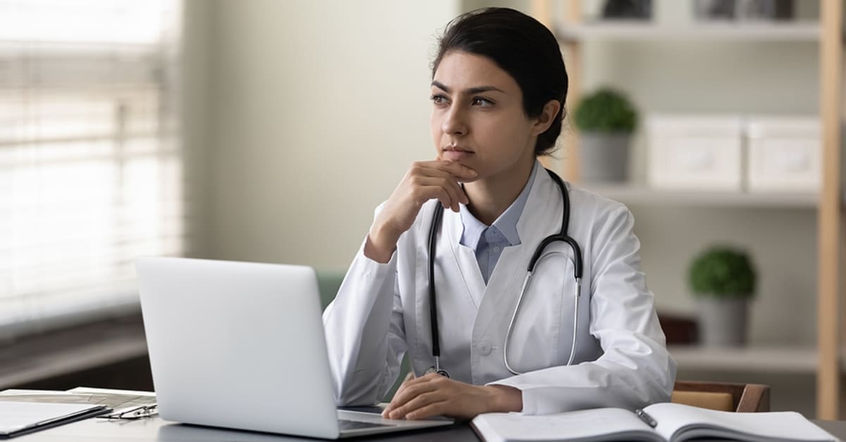 Female Physician Pondering While Sitting in Front of Laptop