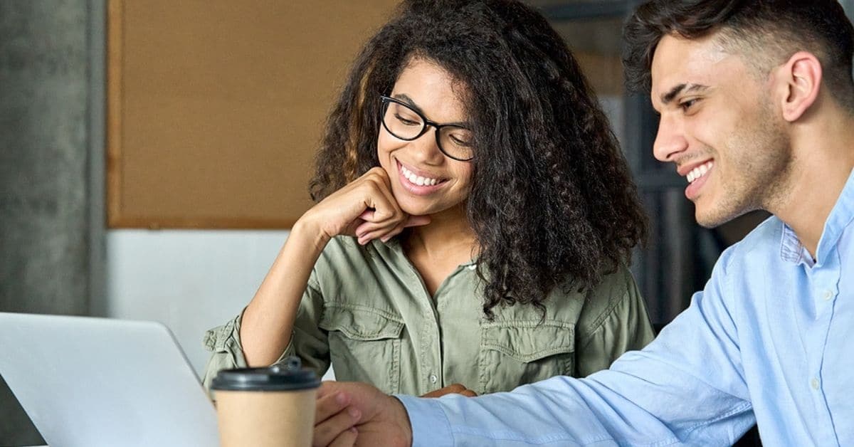 A Man and Woman with Coffee To Go Cup Looking at Laptop Smiling