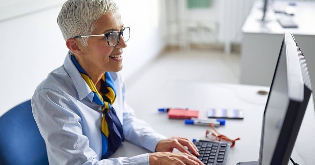 White Blonde Haired Woman Smiling While Typing on Computer