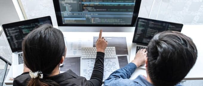 Two Asian Adults Pointing at Three Computers Screens
