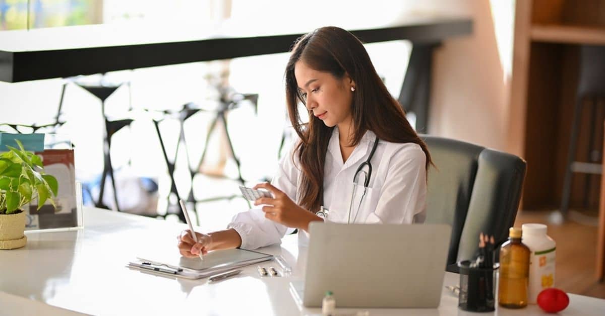 Female Asian Woman Doctor Looking at Blister Packet and Taking Notes