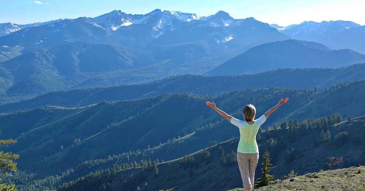 Woman with Arms in the Air Looking at the Expanse of Mountains Ahead