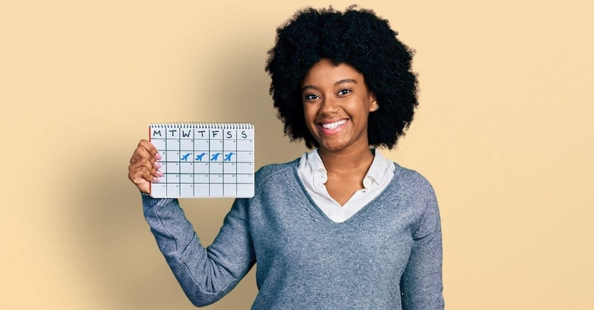 african american woman in gray sweater holding up a calendar in her hand.