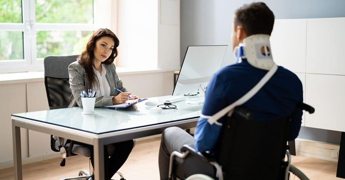 Woman Behind Desk Talking to Man in a Wheelchair