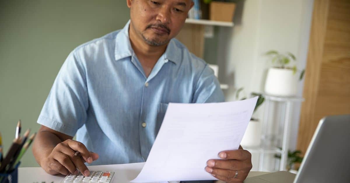 Asian Man Using a Calculator While Looking at Papers