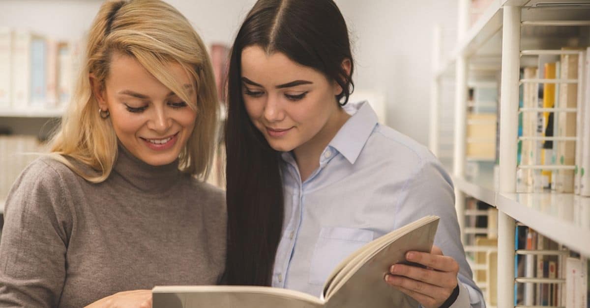 two white women reading book in a library