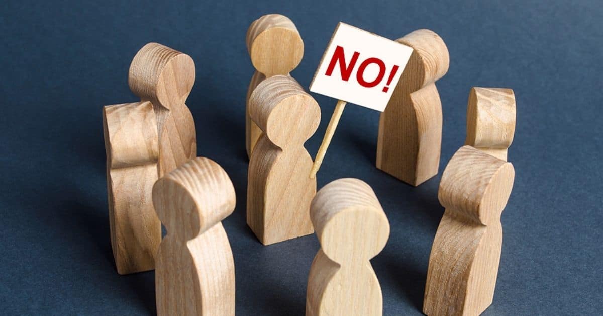 wooden Person holding a NO poster surrounded by people.