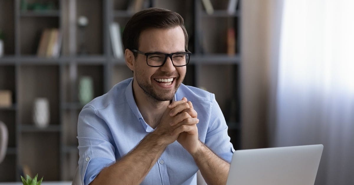 Laughing happy businessman in glasses sitting at work desk