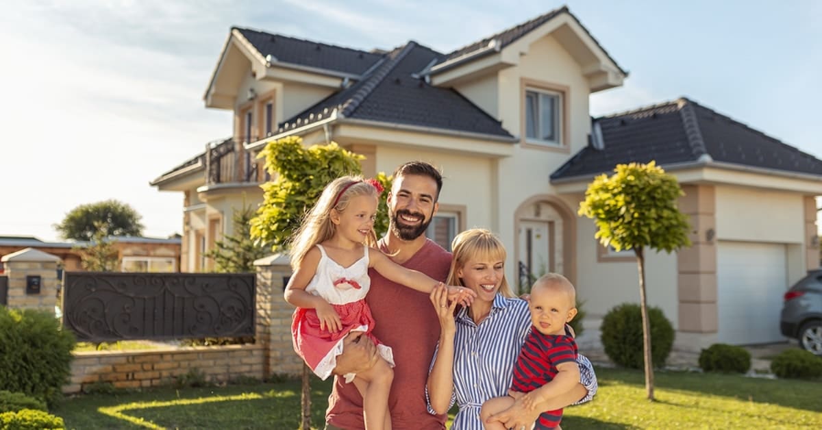 Family buying a new house; parents and children hugging and having fun standing in front of their new house; real estate market and property sales concept
