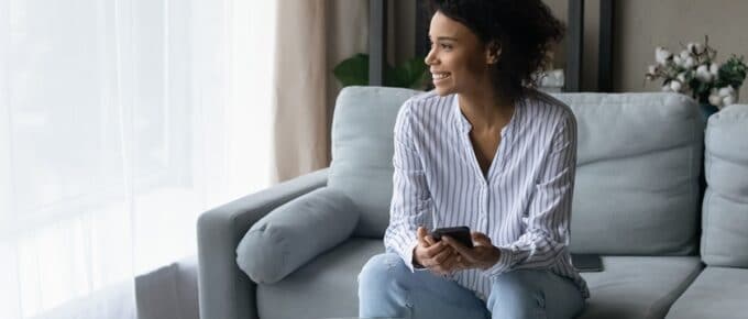 Smiling African American woman calculating bills, sitting on couch