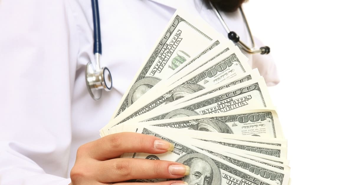 medical doctor holding several 100 dollar bills in hand