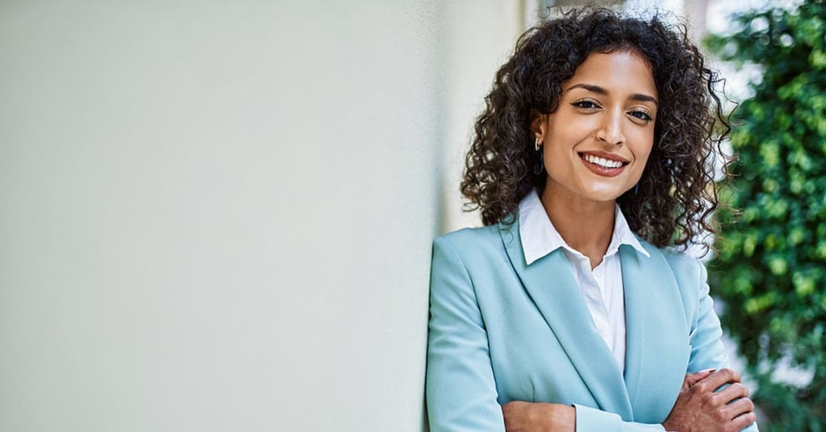 Young hispanic business woman wearing professional look smiling confident at the city leaning on the wall