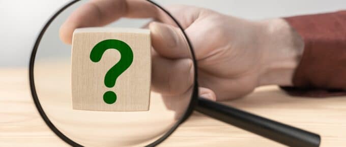 Hand holding question mark in front of magnifying glass. Search for an answer to question. Magnifying glass with question mark in focus on wooden cube. Research, searching or investigating something