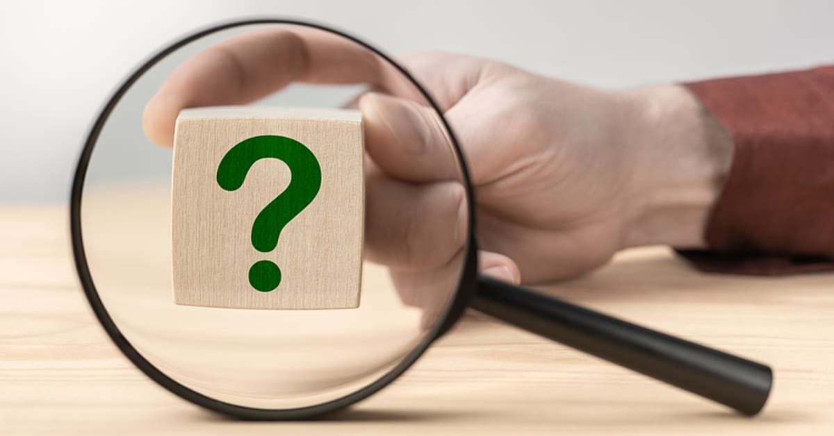 Hand holding question mark in front of magnifying glass. Search for an answer to question. Magnifying glass with question mark in focus on wooden cube. Research, searching or investigating something