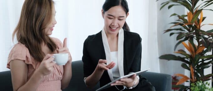 two females on couch having coffee looking at ipad
