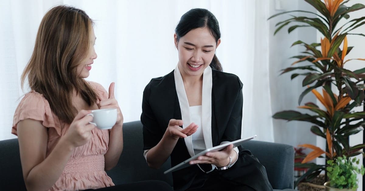 two females on couch having coffee looking at ipad