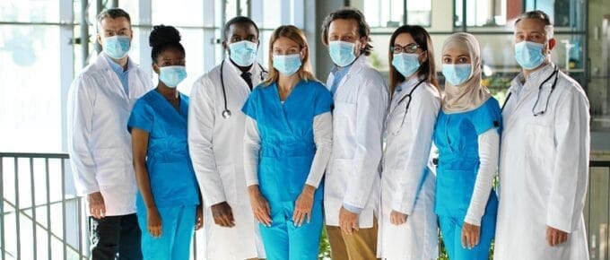 Mixed races team of specialists, males and females doctors in hospital. International group of medics in medical masks. Protected workers. Multi ethnic physicians and nurses in uniforms in clinic.