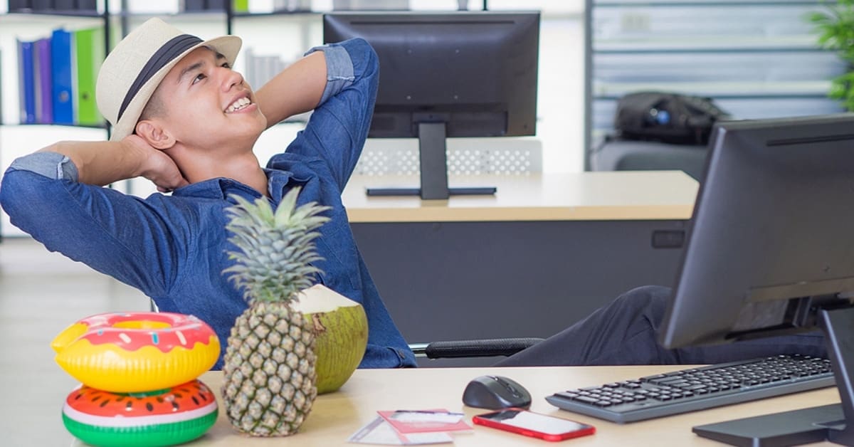 A young man wearing a hat, looking up, placing both hands on the back of the neck and foot on the table for relaxing while sitting on a chair in the office. Holiday coming soon. Holiday concept.