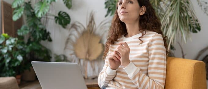 Thoughtful woman holding laptop on lap and sitting on the couch
