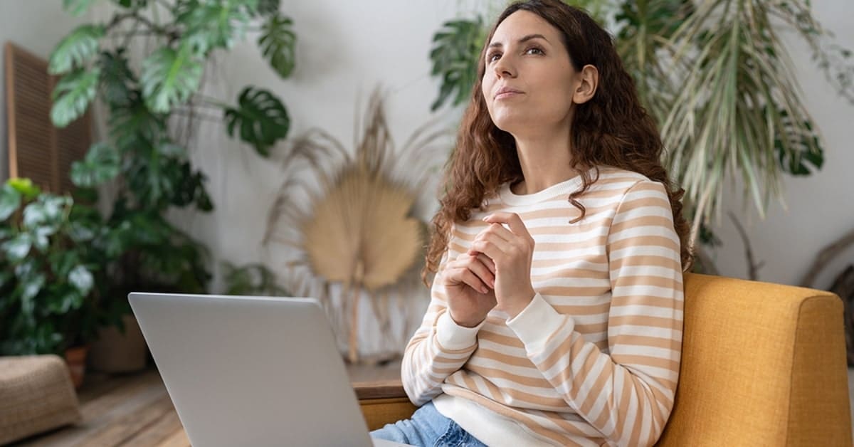 Thoughtful woman holding laptop on lap and sitting on the couch