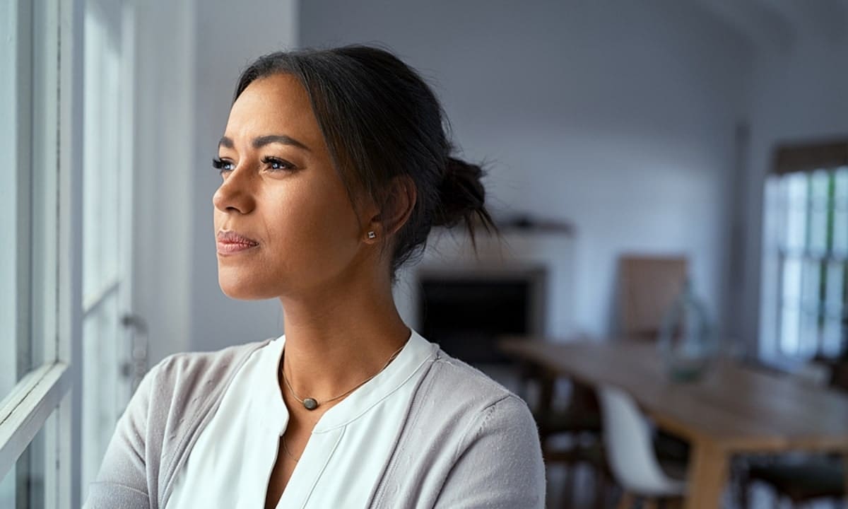 Mature african woman looking outside window with uncertainty.