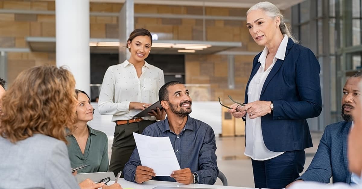 Group of business people discussing work in conference room. Senior business manager guiding employees in meeting. Group of businessman and businesswoman working together while sharing new strategy.