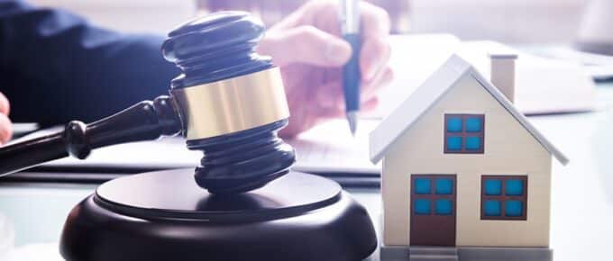 Gavel With Sound Block And House Model Over Desk In Front Of A Businessperson