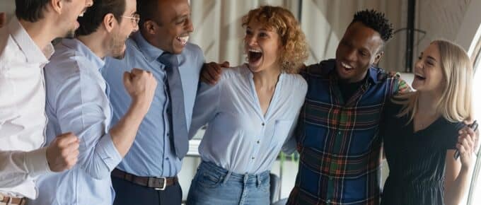 Group of happy excited diverse employees hugging, shouting for joy