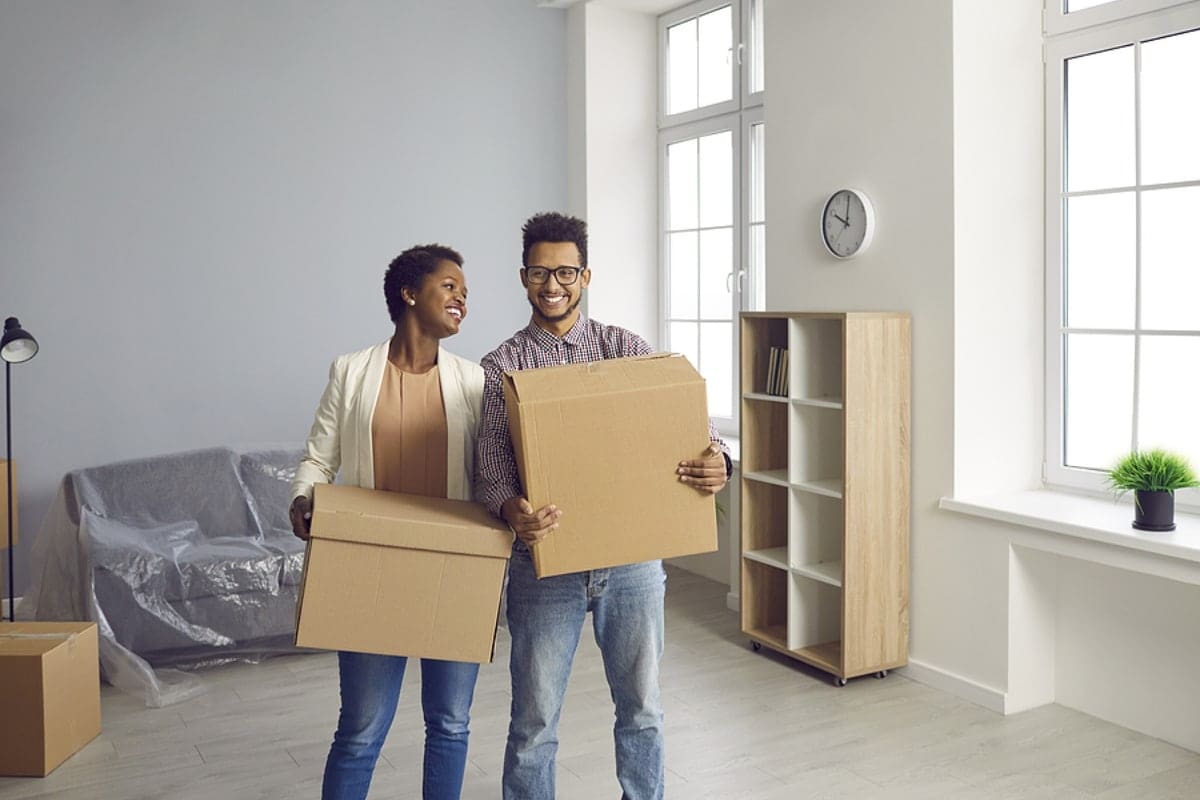 Happy black couple moving into their new house or apartment and carrying boxes together