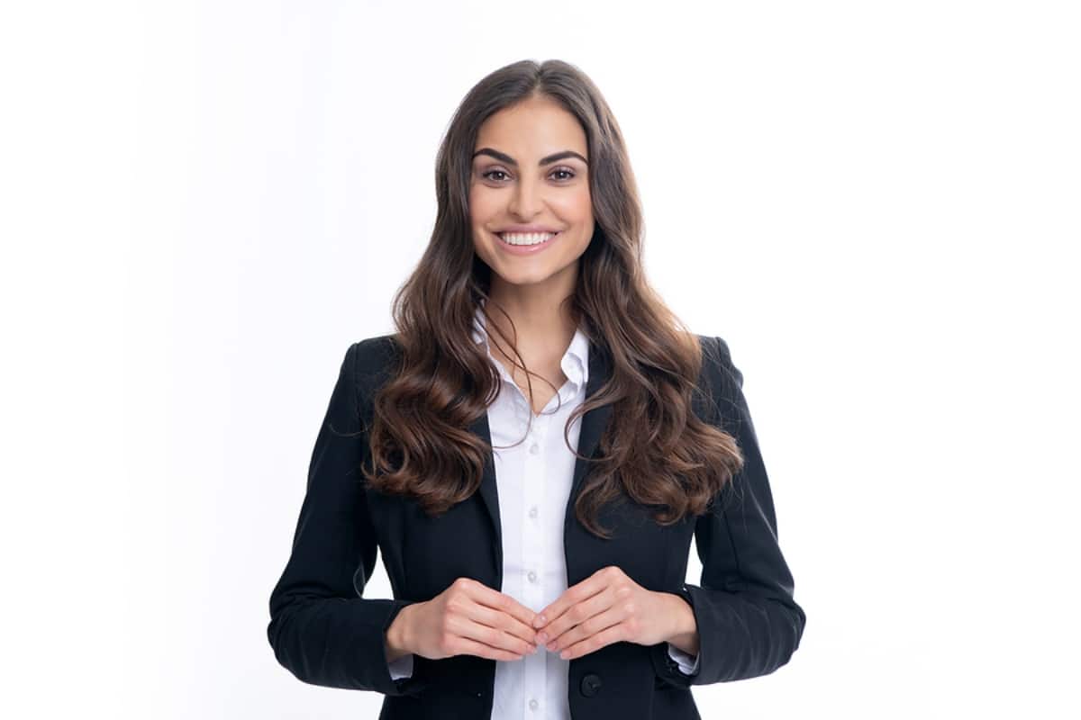 woman with brown hair and black business suit smiling in front of a white background.