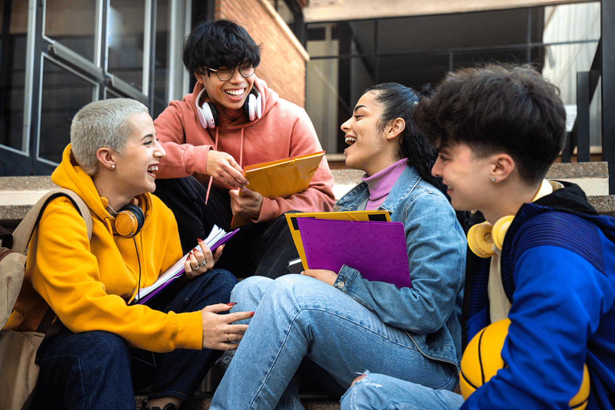 group of college kids sitting on cement steps talking with college in the background