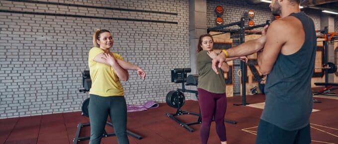 2 women and their trainer stretching hands before sports training in gym.
