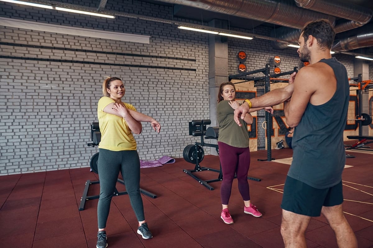 2 women and their trainer stretching hands before sports training in gym.