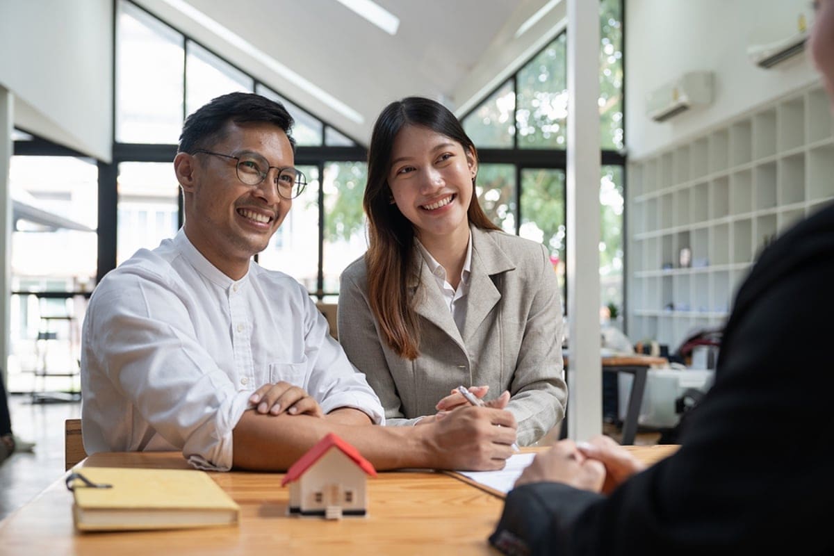 Happy property owners with real estate broker after a deal. Young couple handshaking real estate agent after signing contract.