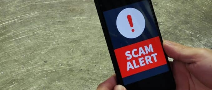 Closeup of male hand holding smartphone with text SCAM ALERT on the screen.