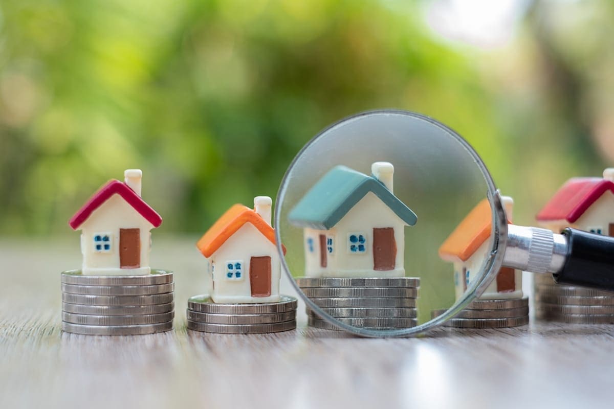 A magnifying glass placed near the house model placed on a pile of coins