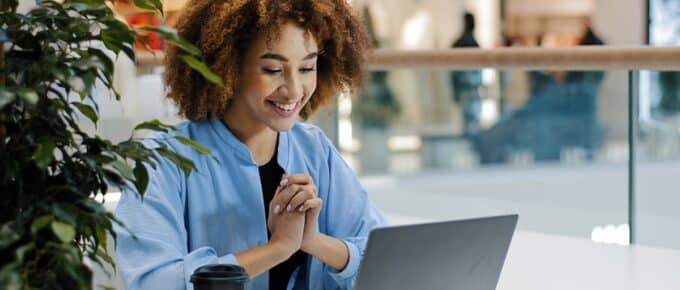 African american girl student using laptop while sitting at a desk and drinking coffee